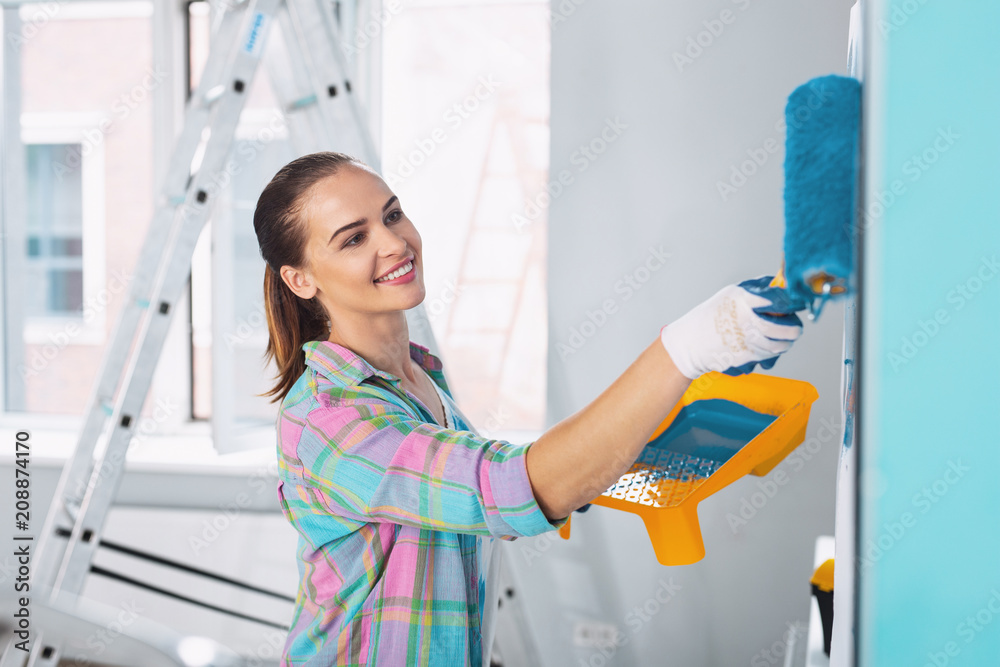 Interesting idea. Exuberant slim woman painting the wall in blue colour and wearing gloves Interesting idea. Exuberant slim woman painting the wall in blue colour and wearing gloves