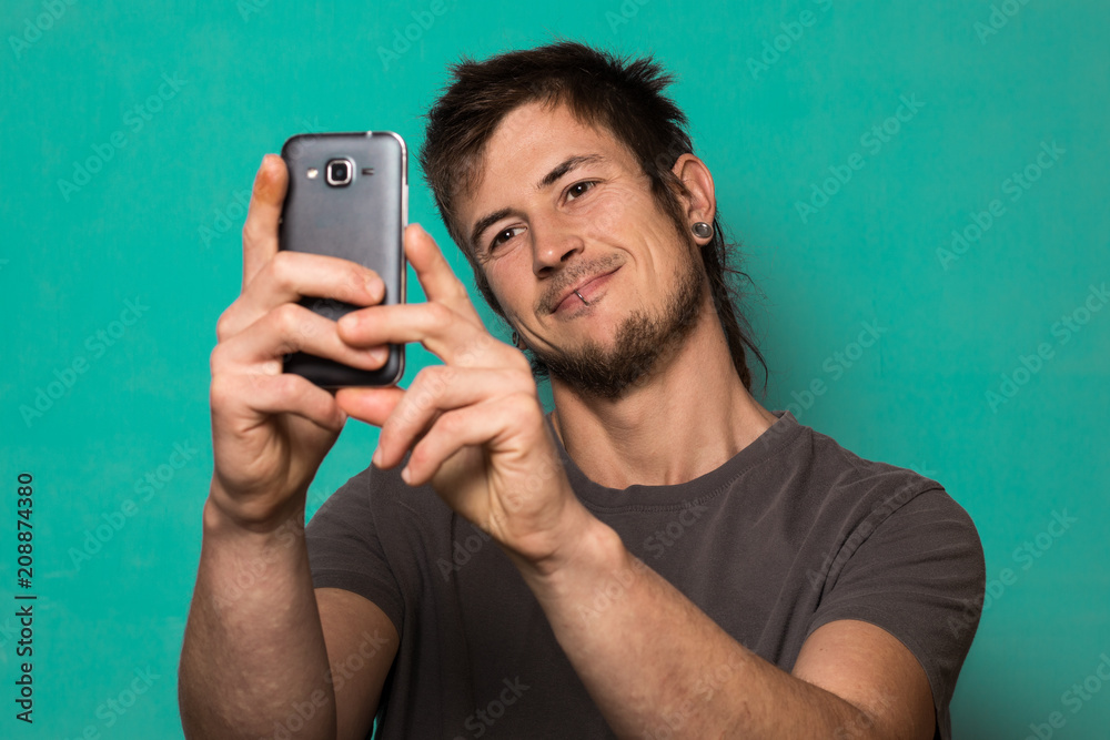 Guy making a selfie with funny faces. Guy taking pictures with his smartphone Guy making a selfie with funny faces. Guy taking pictures with his smartphone