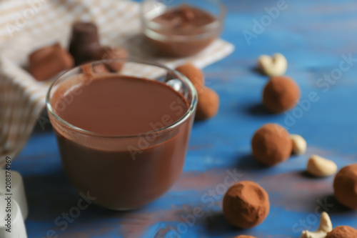 Glass cup of tasty hot chocolate with candies on color wooden background