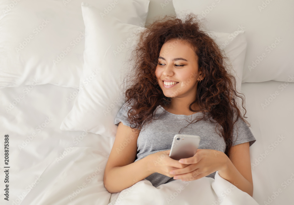 Morning of young African-American woman lying in bed with mobile phone Morning of young African-American woman lying in bed with mobile phone