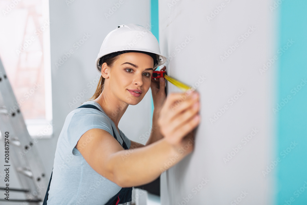 Good design. Concentrated professional builder wearing a uniform and holding a measuring tape Good design. Concentrated professional builder wearing a uniform and holding a measuring tape