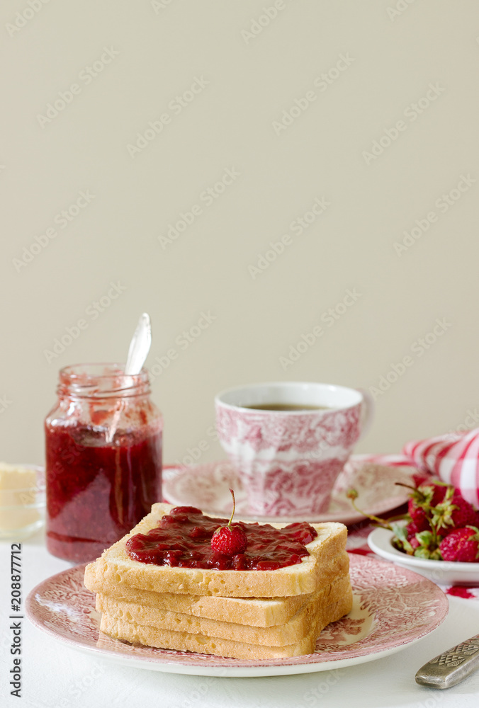 Breakfast of bread toasts with butter and strawberry-rhubarb jam, served with tea. Rustic style. Breakfast of bread toasts with butter and strawberry-rhubarb jam, served with tea. Rustic style.