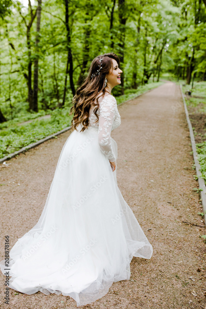 An emotional girl in a white dress walks along the path in the park