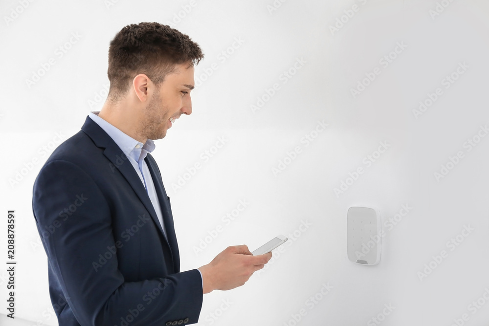 Young man with phone near security system indoors Young man with phone near security system indoors