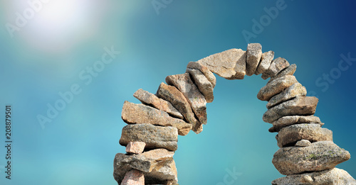 Leinwand Poster stone cairn forming arc on sunny blue sky
