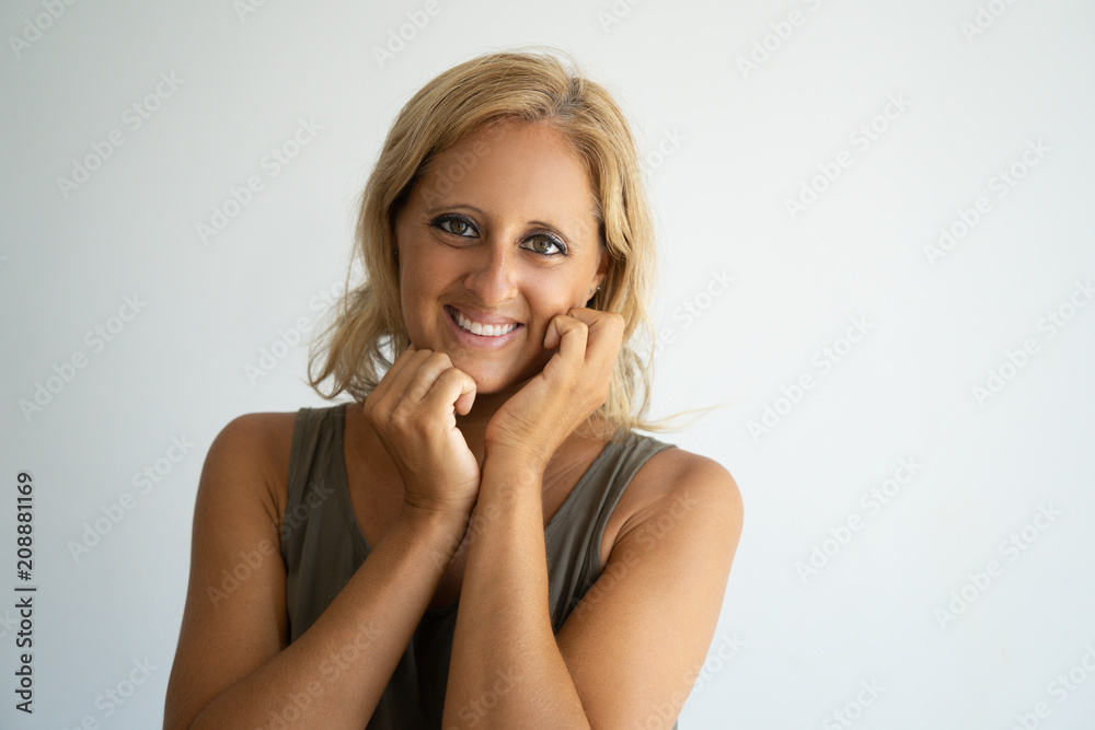 Fototapeta premium Cheerful blonde lady happy about new cosmetic product and smiling at camera. Closeup of attractive Caucasian woman keeping hands at face and posing. Positive emotions and skin care concept