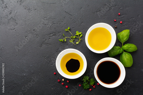 Soy sauce, olive oil and balsamic sauce with herbs basil, parsley, pepper and thyme in white ceramic bowls on black stone or concrete background.