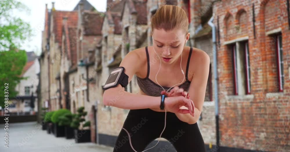 Tired woman jogger stopping to breathe and check her smartwatch, Athletic woman listening to music on smartphone while running, 4k