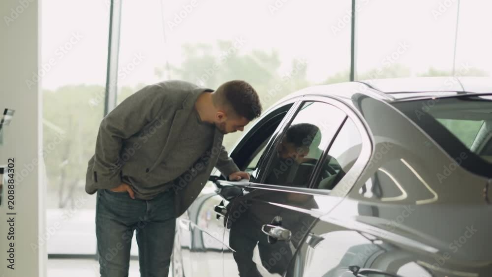 Stylish guy is choosing new automobile walking around luxury car and touching it in car dealership. Rich people, transportation and business class vehicles concept. Stylish guy is choosing new automobile walking around luxury car and touching it in car dealership. Rich people, transportation and business class vehicles concept.