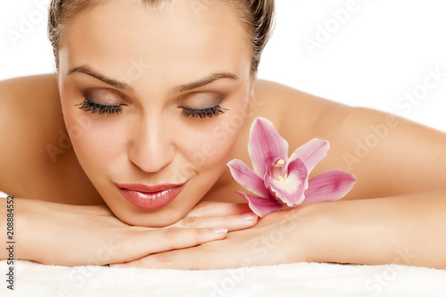 a pretty young woman lying with orchid on a white background