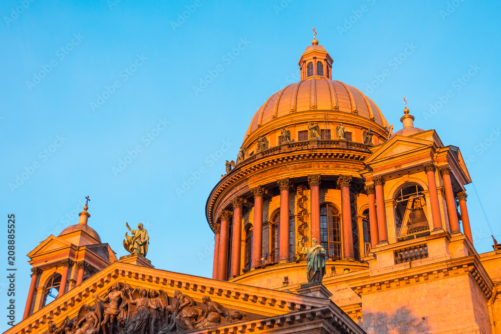 Saint Isaac's Cathedral in the square, in St. Peterburg in the evening on a bright orange sunset sky.