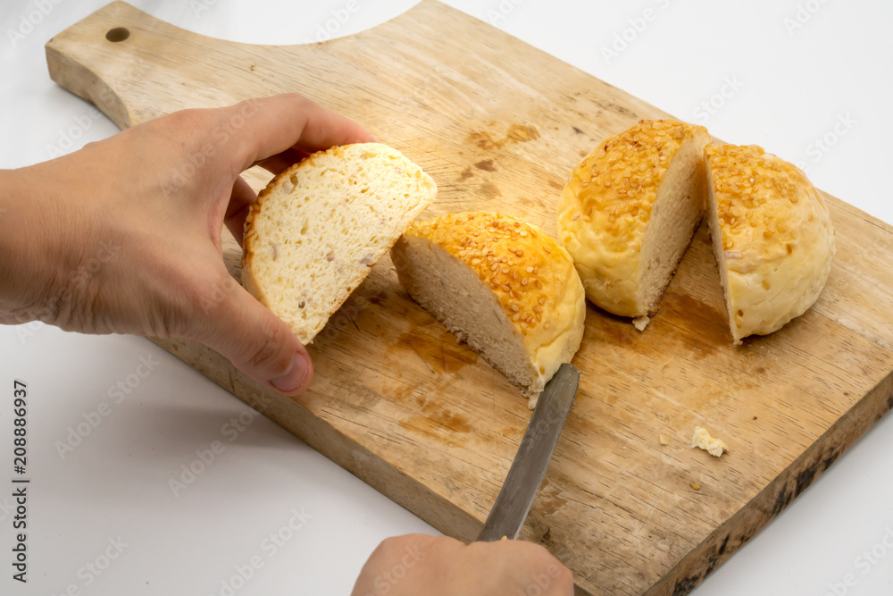 Hand cutting whole bun with sesame seeds on wooden square cutting board isolated on white Hand cutting whole bun with sesame seeds on wooden square cutting board isolated on white