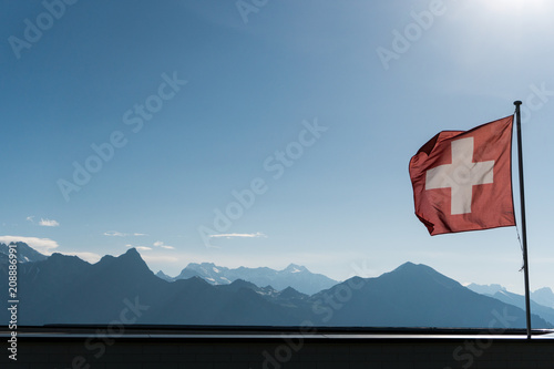 Swiss flag blowing in the wind with a gorgoues mountain landscape and blue sky behind