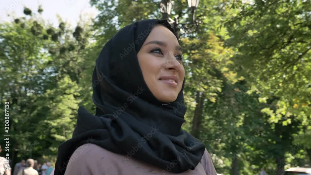 Young happy muslim girl in hijab is smiling and watching at university in daytime in summer, religious concept, studying concept