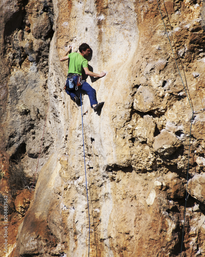 Man rock climber. Rock climber climbs on a rocky wall. Man makes hard move. Man rock climber. Rock climber climbs on a rocky wall. Man makes hard move.