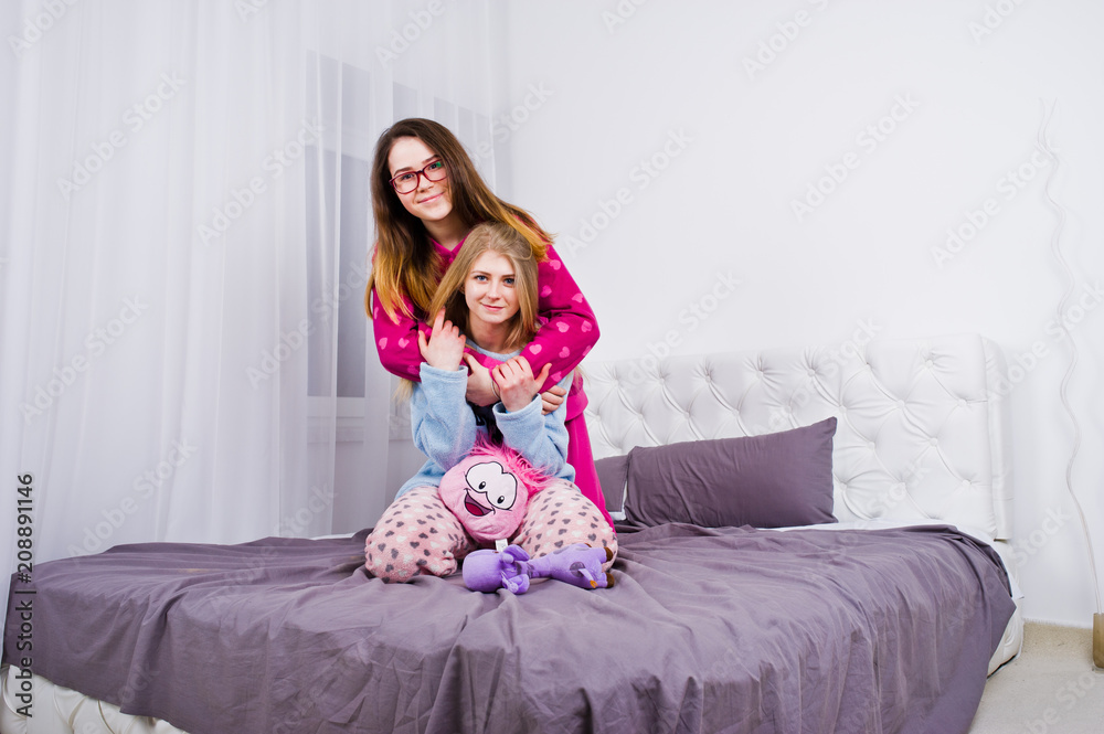 Two friends girls in pajamas having fun on bed at room.
