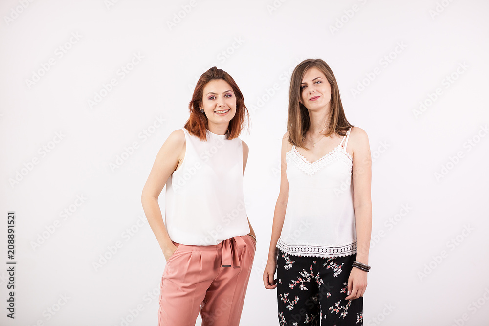Two girl friends smiling on white wall in studio photo Two girl friends smiling on white wall in studio photo