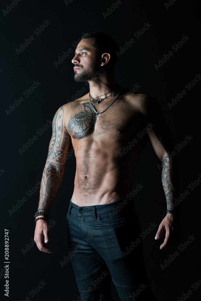 Fototapeta premium Bodycare with fitness and sport. Tattooed man show sexy muscular torso. Sportsman with six pack and ab. Bodybuilder with biceps and triceps. Fashion model with tattoo in jeans