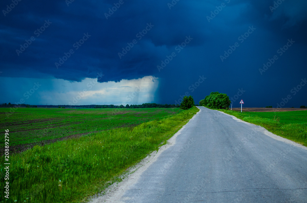 The asphalt road goes into the distance. Way to the next village. Storm clouds are approaching