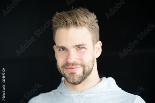 Man with bristle on smiling face, black background. Metrosexual concept. Man with beard or unshaven guy looks handsome and cool with healthy skin. Guy bearded and attractive cares about appearance