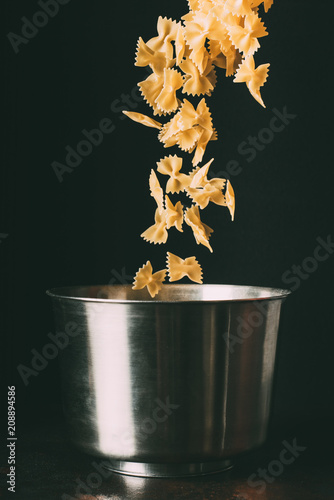 Slika na platnu close up view of farfalle falling into pan on black background