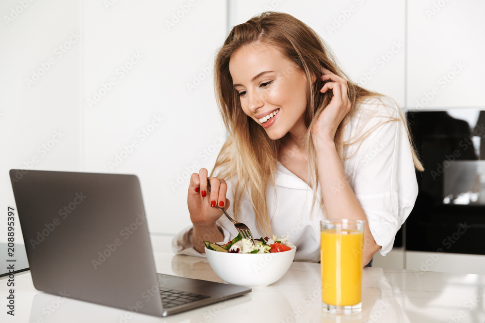 Happy young woman eating salad from a bowl