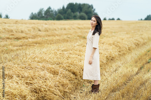 Portrait of Young farmer girl is standing in the middle of row cutted field of hay. Rural lifestyle concept. Space fot text