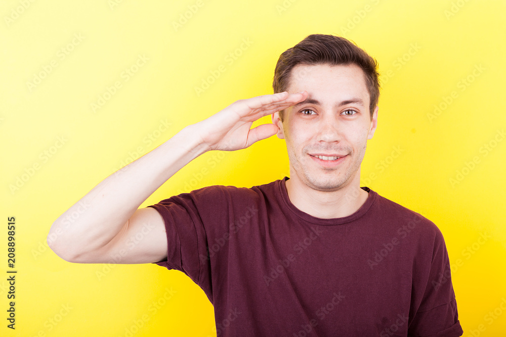 Man with his hand to the forehead making the army salute sign on yellow background in studio photo Man with his hand to the forehead making the army salute sign on yellow background in studio photo