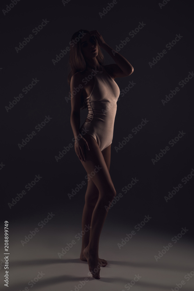 Naklejka premium Adore frilly lingerie! Full length portrait of the attractive young lady with sexy body wearing fashionable lingerie standing in the dark photo studio.