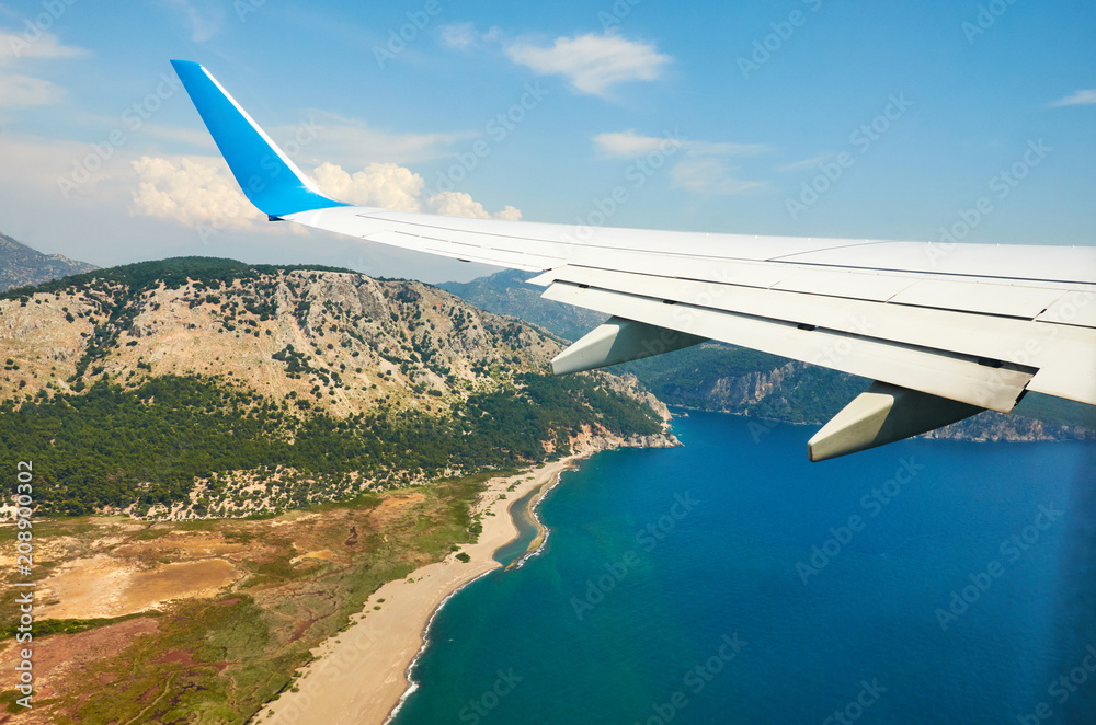 View from airplane window travel tourism. Wing of an airplane flying above the clouds over tropical island Turkey View from airplane window travel tourism. Wing of an airplane flying above the clouds over tropical island Turkey
