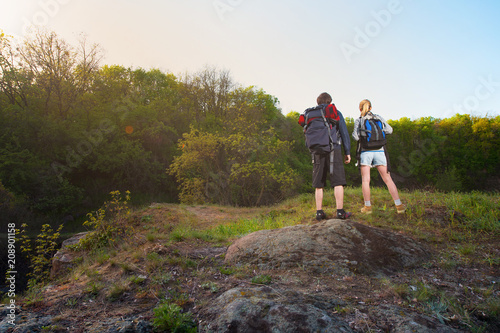 Back view of travelers or hikers stands on mountain top at sunset or sunrise time looking at sky. Travel concept.