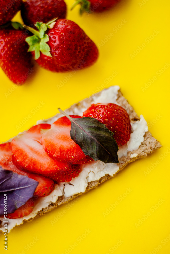 Snack with crispbread, cream cheese, fresh strawberry and basil on a yellow background Snack with crispbread, cream cheese, fresh strawberry and basil on a yellow background