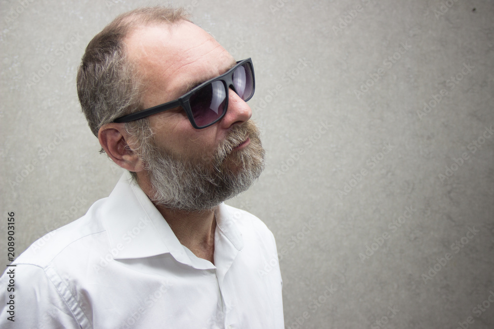 Obraz premium A man in a shirt with a beard in glasses is standing by the wall
