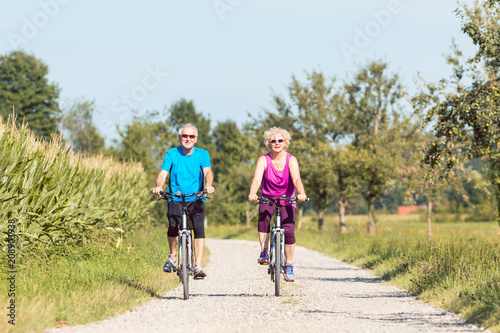 Full length front view of an active senior couple enjoying retirement while riding bicycles in a sunny day of summer in the countryside