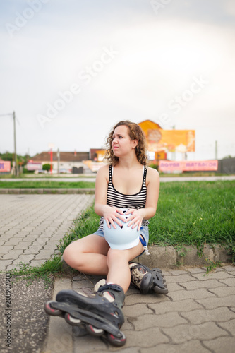 Beautiful curly woman sitting in car park with her inline roller skate and helmet for safety sport