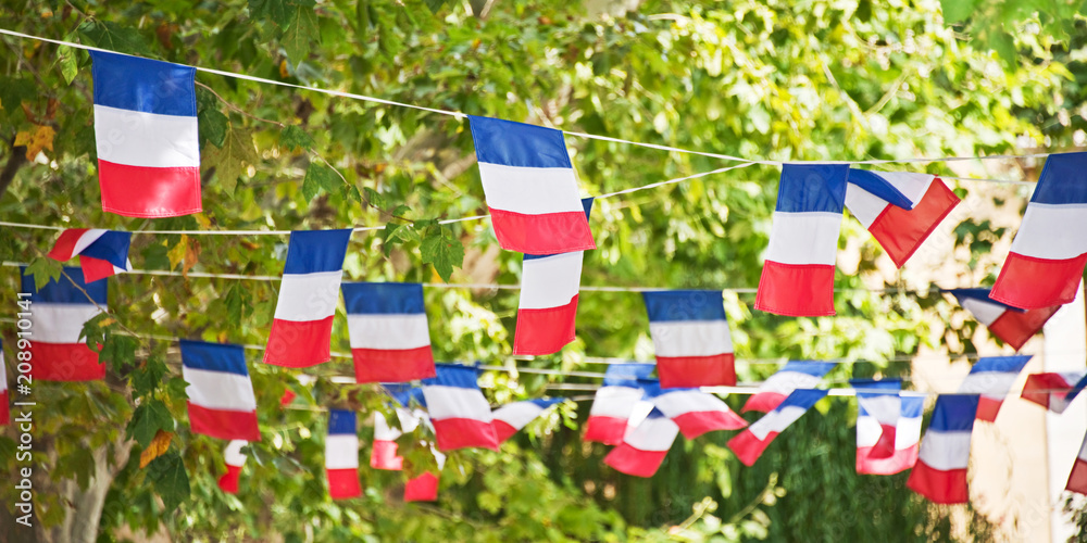 Fototapeta premium Blue white red strings of french flags, patriotic banner, decorating a village square, July 14 party, National Day celebration panoramic web banner