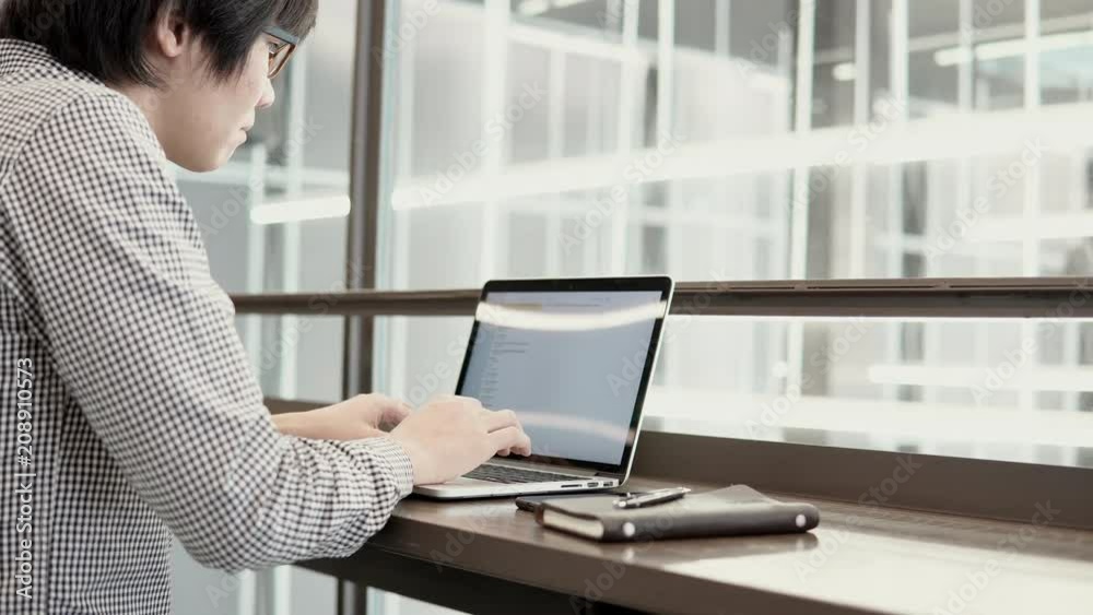 Young Asian business man using laptop computer and smartphone on wooden desk in working space. Male hand typing on laptop keyboard. Freelance lifestyle in digital age concept. 4K video Young Asian business man using laptop computer and smartphone on wooden desk in working space. Male hand typing on laptop keyboard. Freelance lifestyle in digital age concept. 4K video