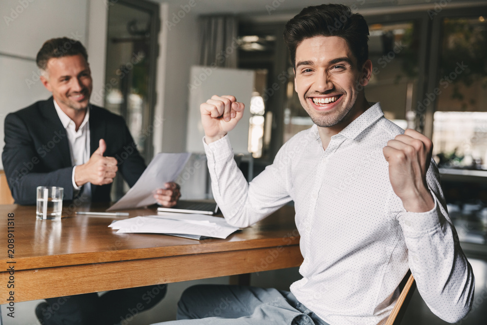 Career, office and placement concept - successful caucasian man 30s rejoicing and clenching fists, during job interview with employee of big company Career, office and placement concept - successful caucasian man 30s rejoicing and clenching fists, during job interview with employee of big company