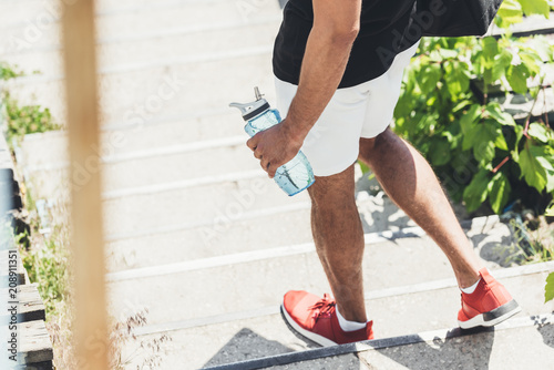 cropped image of sportsman holding bottle of water on stairs at sport playground