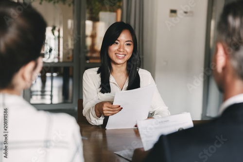 Business, career and recruitment concept - young asian woman smiling and holding resume, while interviewing as candidate for job in big company photo