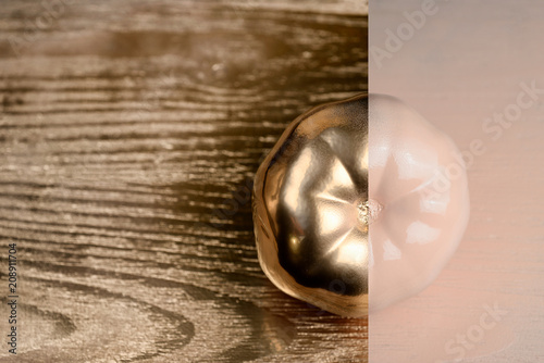 Gold and beige or ecru half painted tomato on golden and wooden background.