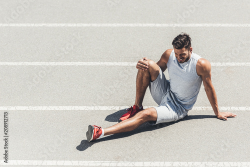 Fototapeta Naklejka Na Ścianę i Meble -  fit young jogger with leg injury sitting on running track