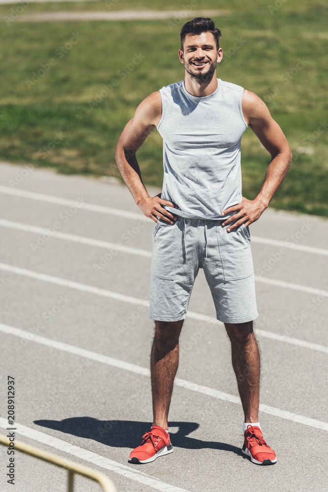 happy young man standing on running track with arms akimbo happy young man standing on running track with arms akimbo