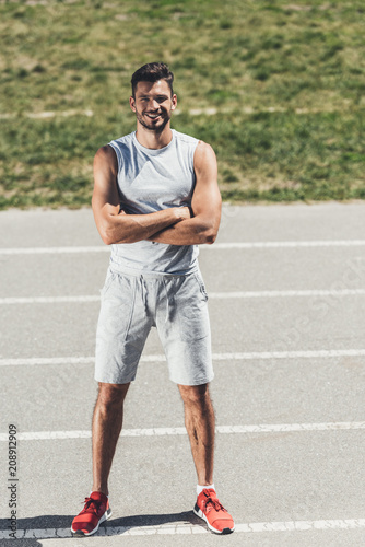 smiling sporty young man with crossed arms looking at camera on running track