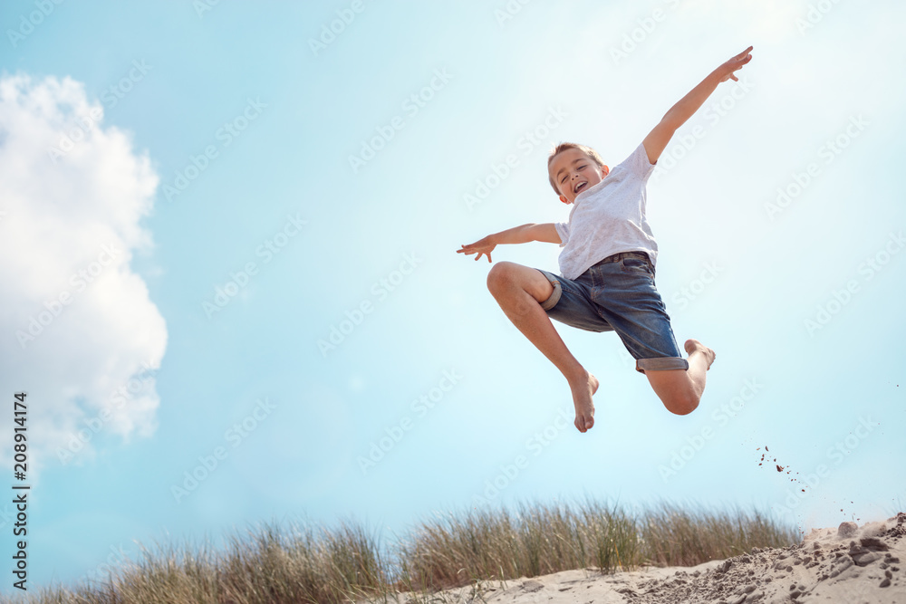 Boy running and jumping over sand dune on beach vacation Boy running and jumping over sand dune on beach vacation