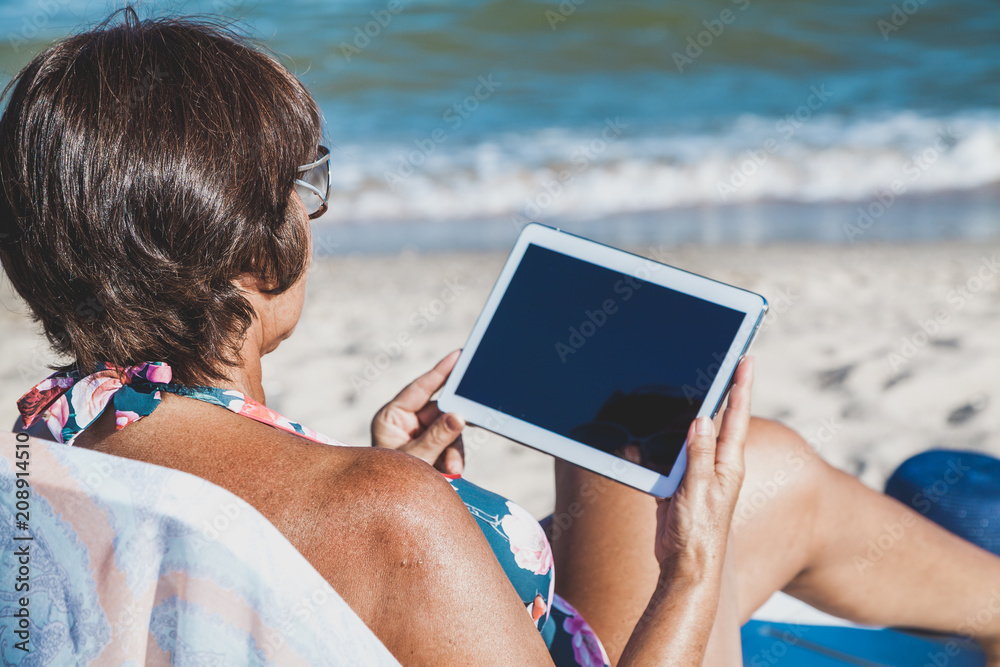 Elderly woman with tablet on beach