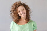 Headshot Young cheerful happy curlyhair ginger girl smiling broadly and looking at camera over gray background. European shaggy hirstyle female have good mood and pleasant face. People concept