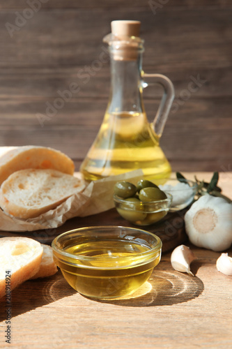 Bottle of olive oil with fresh bread and garlic on wooden table