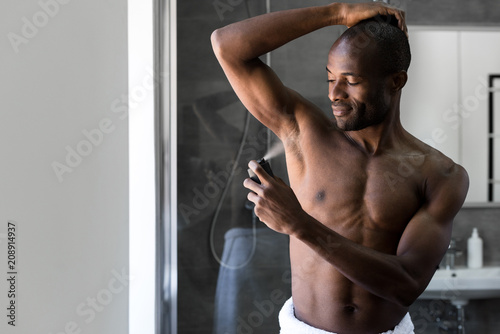 smiling african american man in towel holding deodorant spray in bathroom photo