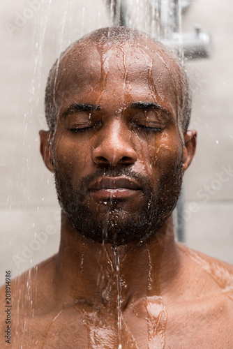 close-up view of young african american man washing in shower with closed eyes